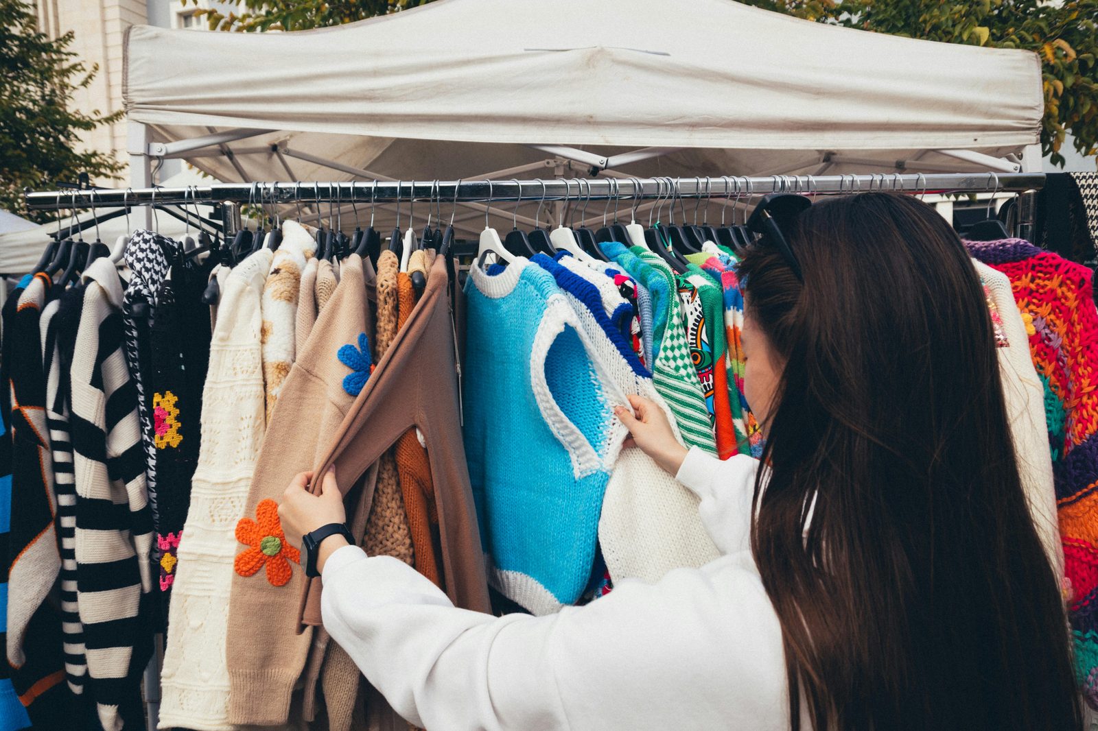 A woman browsing colorful vintage sweaters at an outdoor market — Copenhagen has one of Europe's best vintage shopping scenes across Ravnsborggade, Elmegade and Jægersborggade