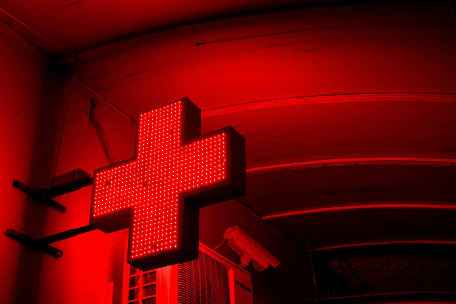 A glowing red cross pharmacy sign on a European street — dial 112 for emergencies in Denmark and know your nearest 24-hour apotek