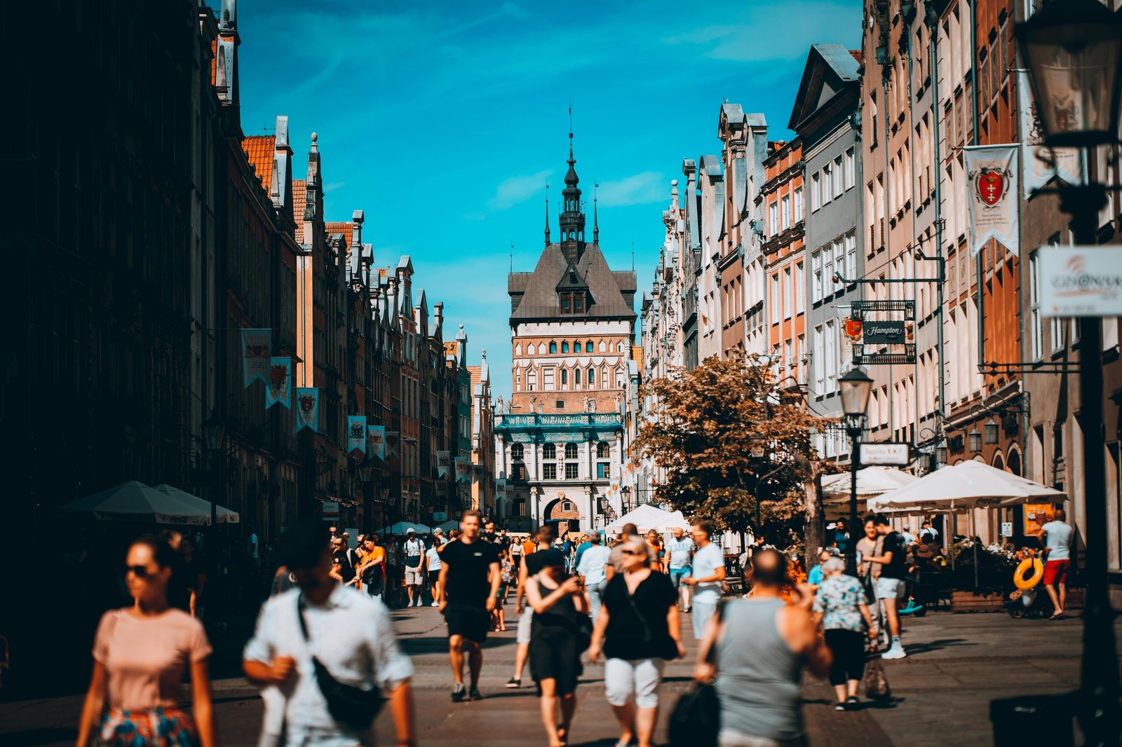 Pedestrians strolling on a sunny cobblestone street in a European old town — similar to Copenhagen's Strøget walking street on a weekend