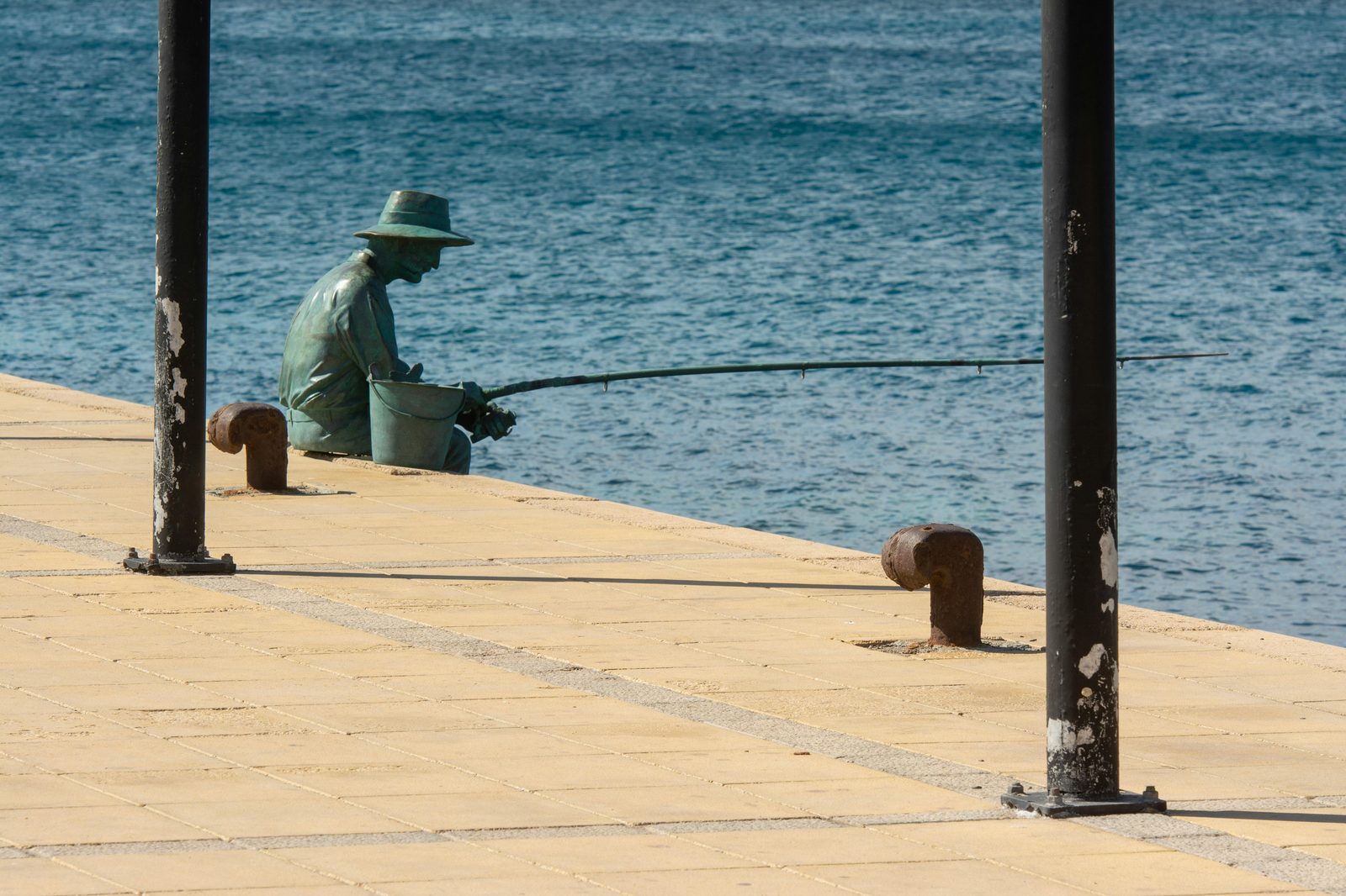 A bronze statue on a seaside promenade framed by posts — the Little Mermaid statue has stood on its boulder at Langelinie since 23 August 1913