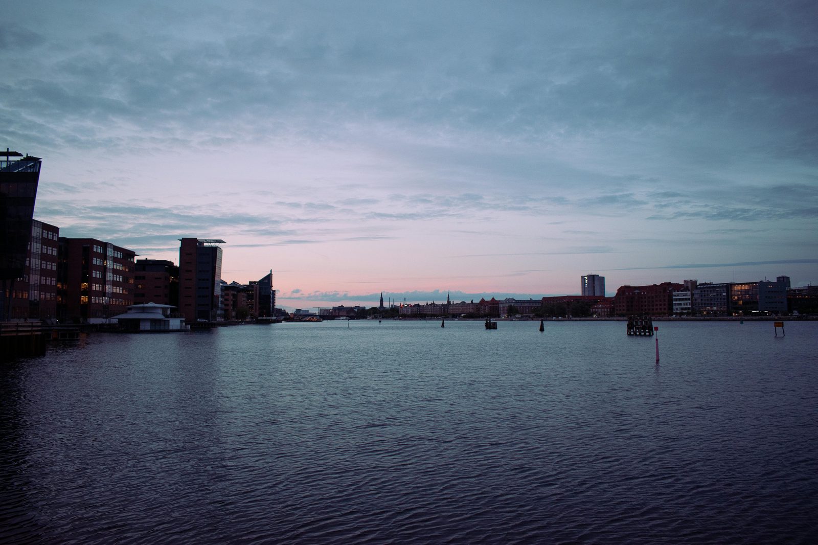 Panoramic view of Copenhagen's waterfront skyline at dusk — the Little Mermaid statue at sunset is the photographer's secret window