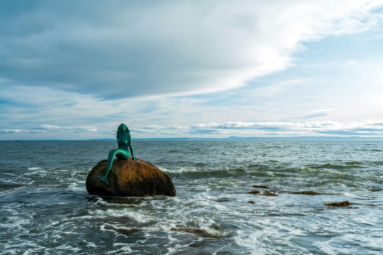 Serene view of a mermaid statue perched on a rock in a vast ocean landscape — Copenhagen's Little Mermaid statue is the most photographed sculpture in Denmark