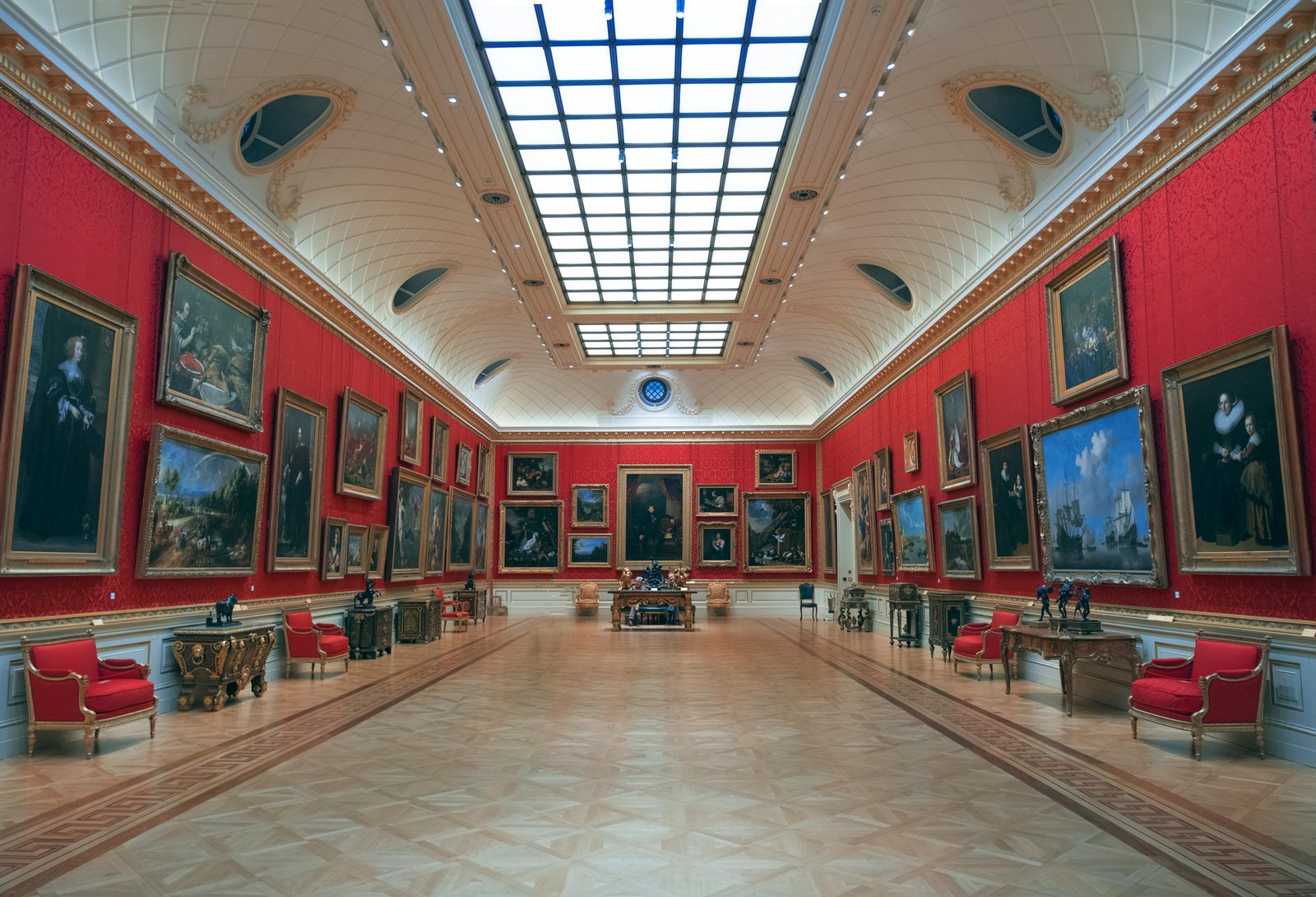 Elegant art gallery in London displaying classic paintings on red walls under skylit ceiling — the National Museum's Renaissance and Baroque rooms display royal portraits and Danish painting