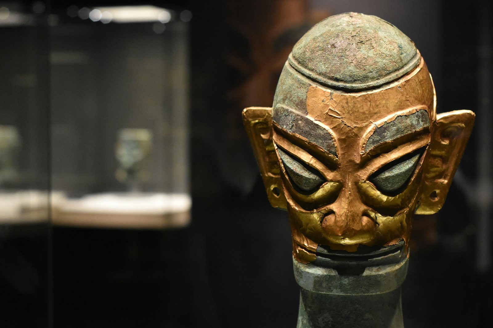 Close-up of an ancient bronze mask exhibited in a dimly lit museum display case — the National Museum holds Denmark's most important Viking and prehistoric collections