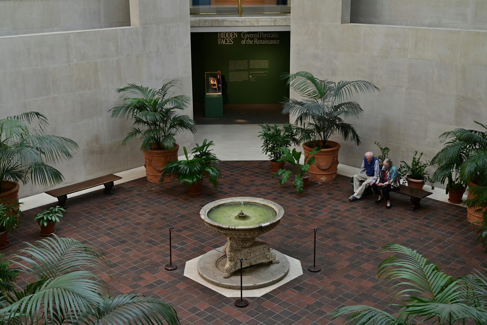 A tranquil indoor museum atrium with a central fountain and seating area — the Glyptotek's main entrance hall combines marble, brass and 19th-century sculpture