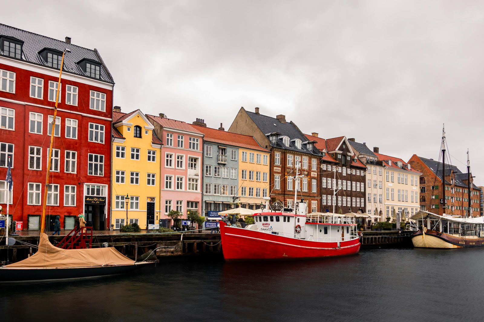 Colorful buildings lining Nyhavn Canal with boats docked and diners at quayside tables — Nyhavn's terrace restaurants are Copenhagen's most iconic summer dining