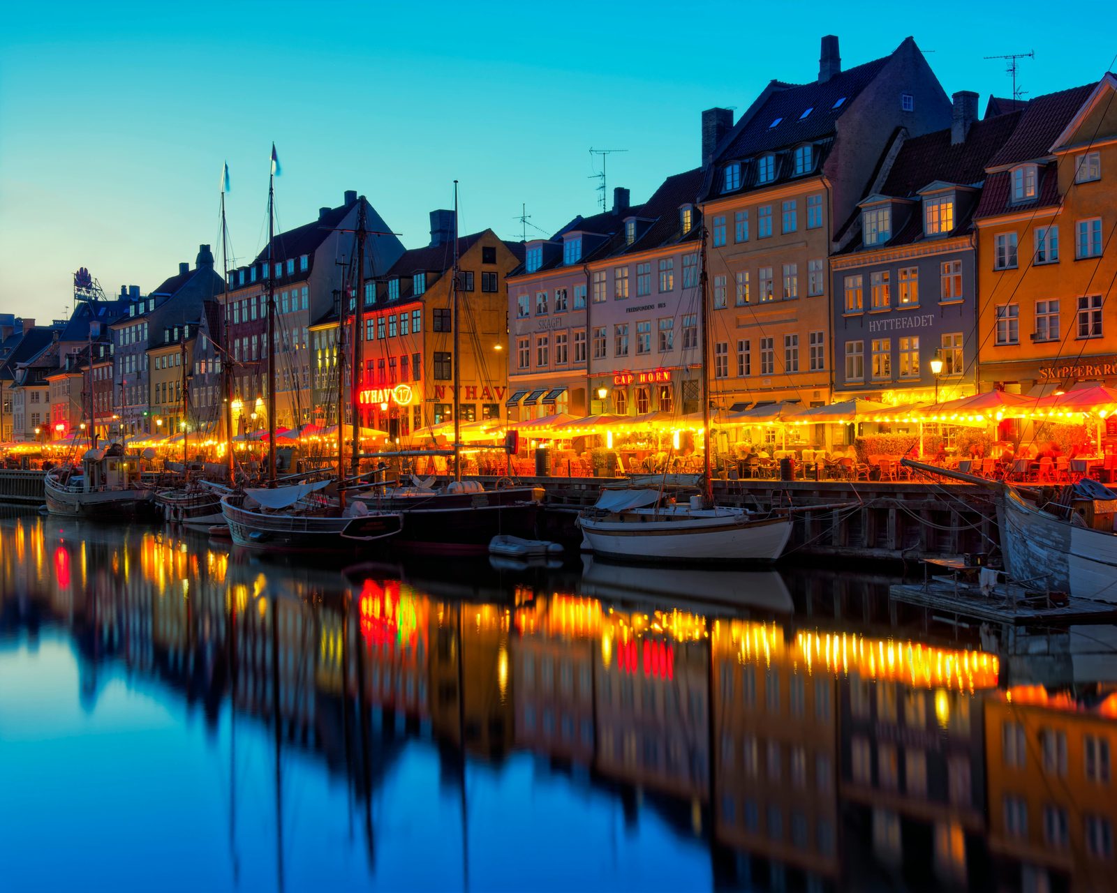 Beautiful view of Nyhavn Canal with illuminated buildings and boats at dusk in Copenhagen — summer evenings are the golden hour for photography
