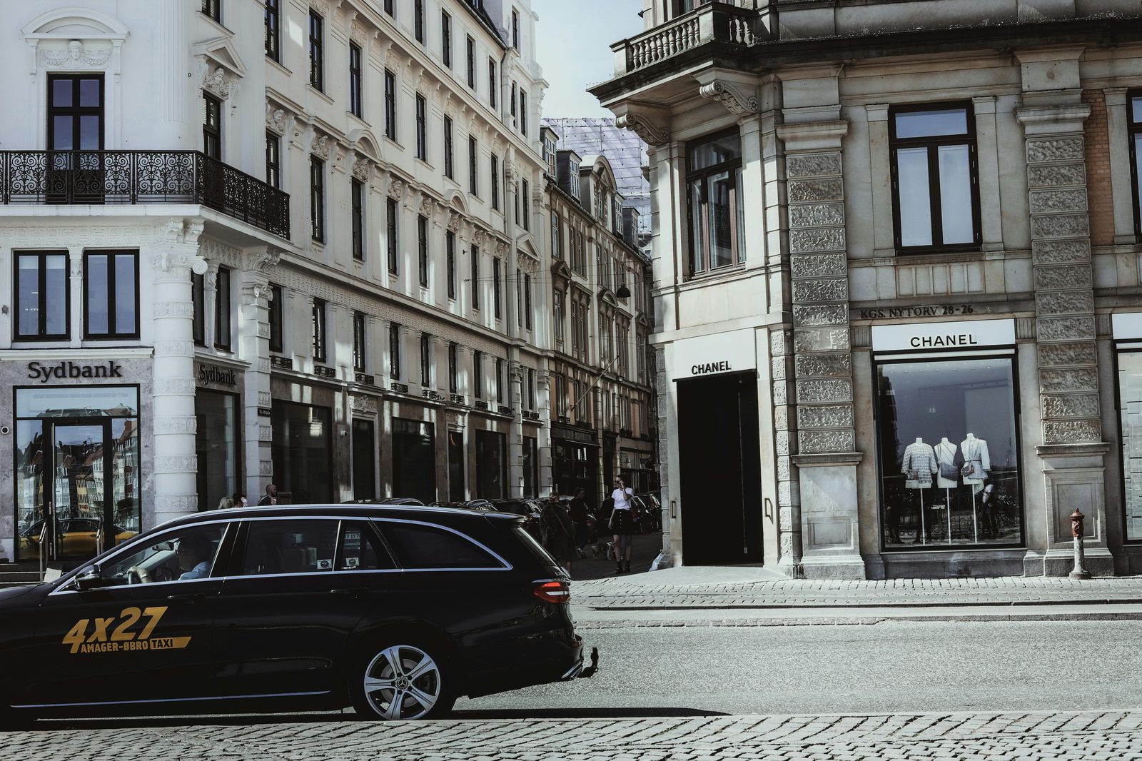 A bustling street corner in Copenhagen featuring elegant architecture and a Chanel storefront — the Round Tower sits 2 minutes off Strøget shopping street