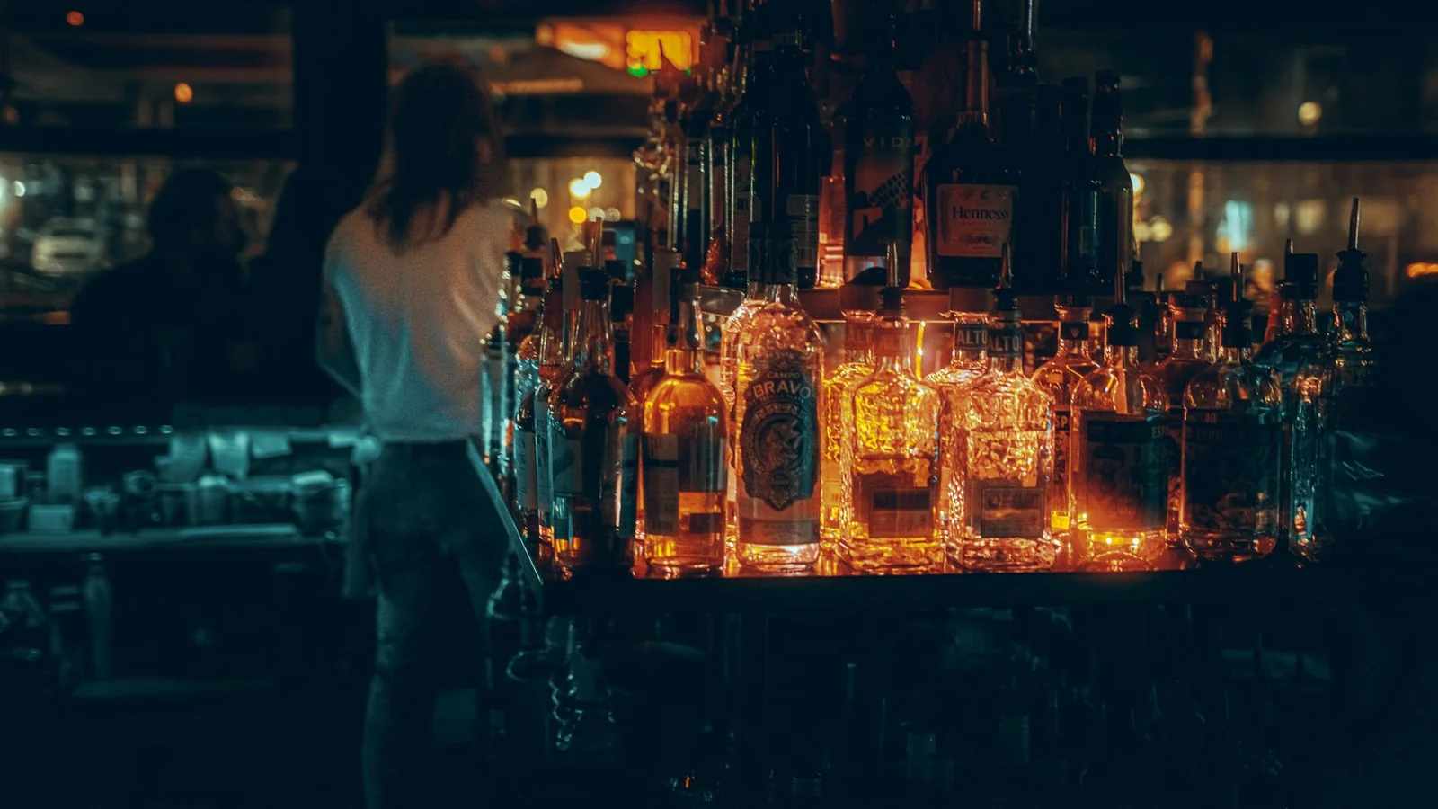 Backlit spirit bottles glowing along the counter of a cocktail bar