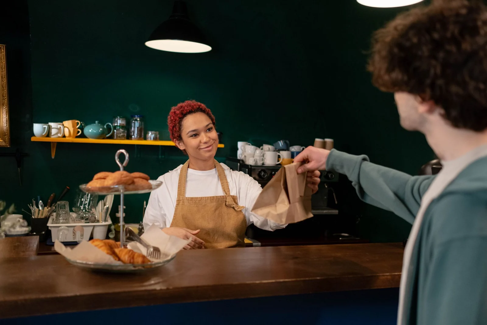 A cafe worker handing a paper bag of pastries across the counter to a customer