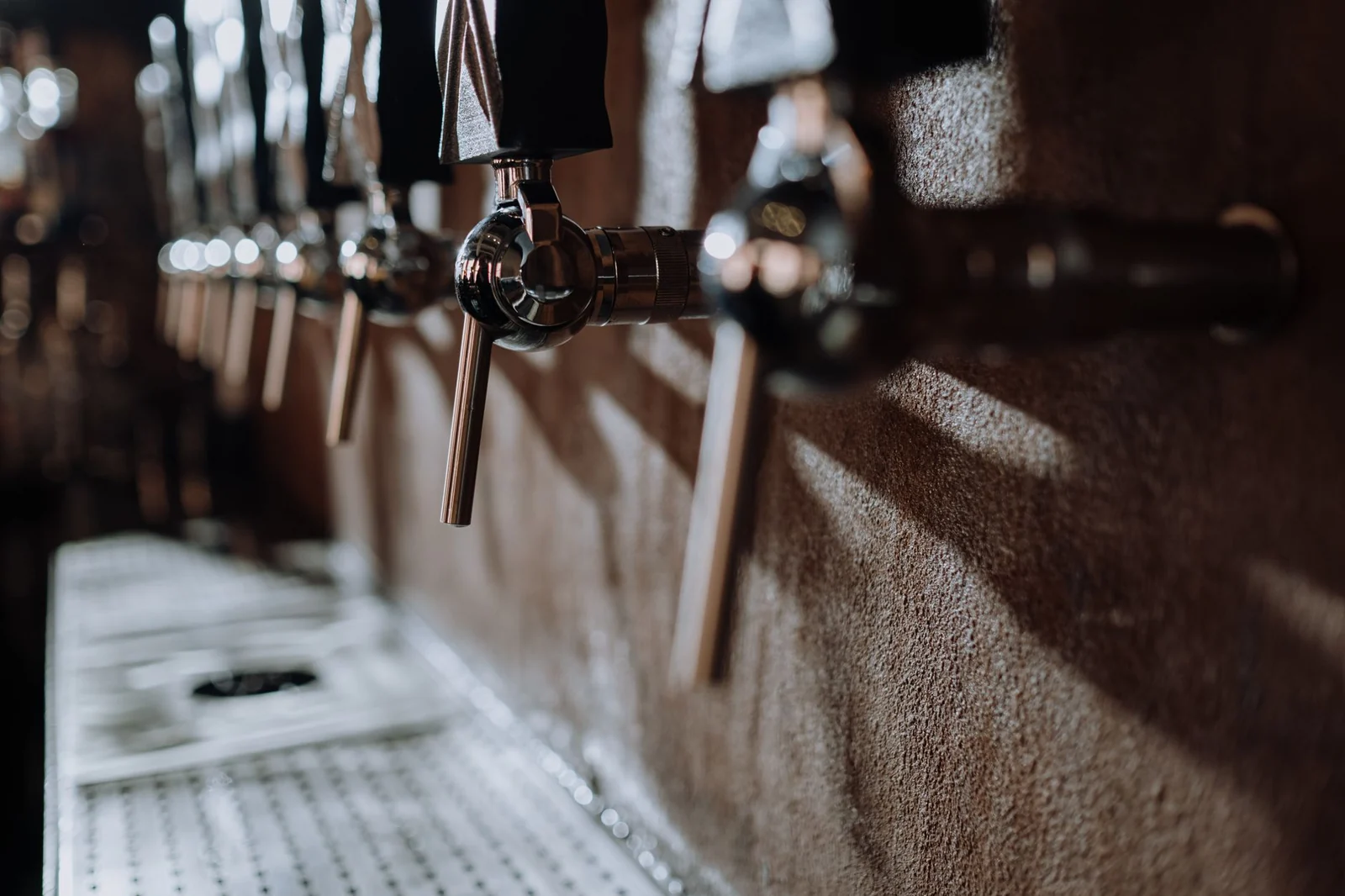Close-up of a row of steel beer taps on a dark bar wall