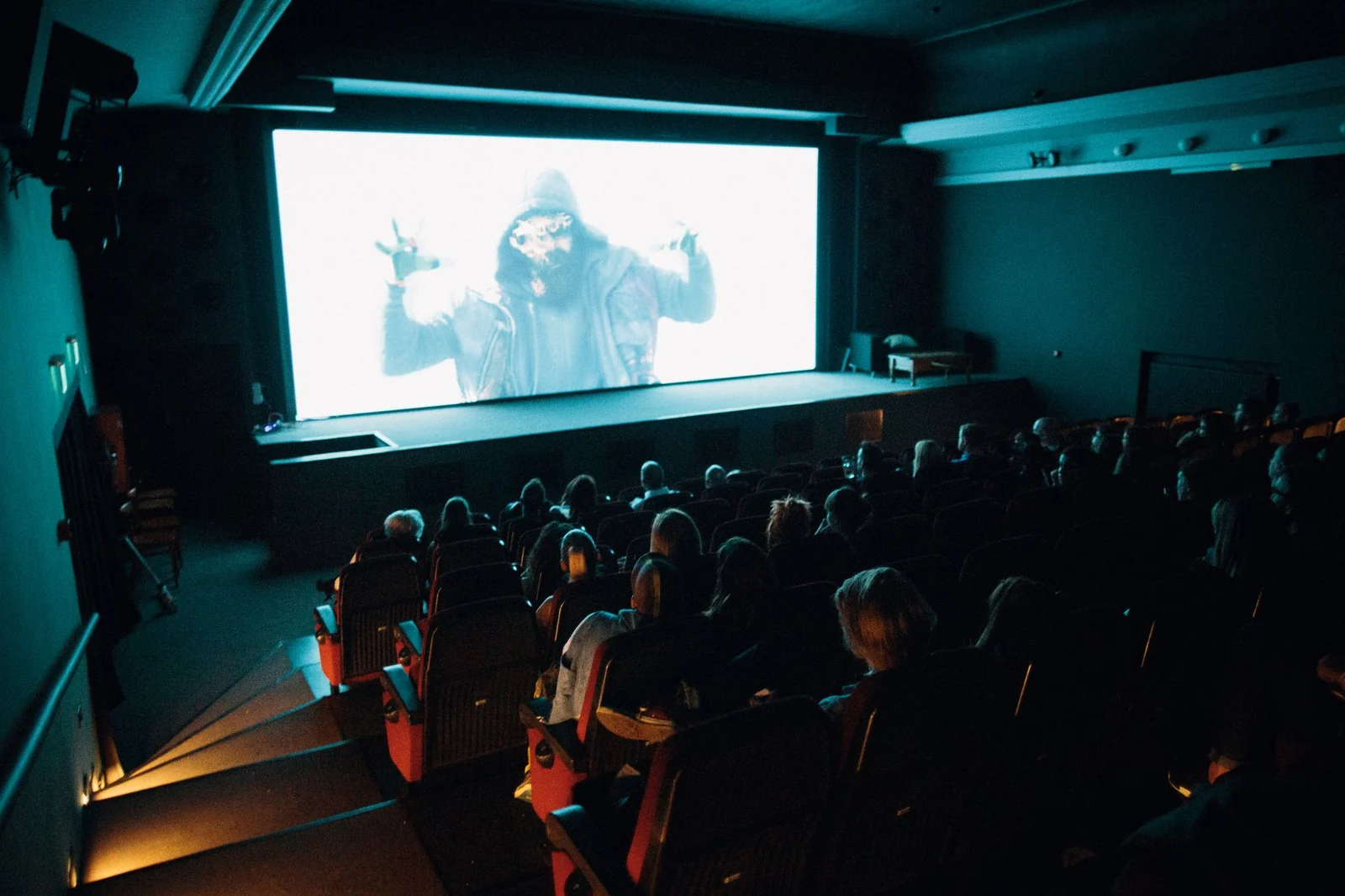 Audience seated in a dark cinema watching a film on a large screen