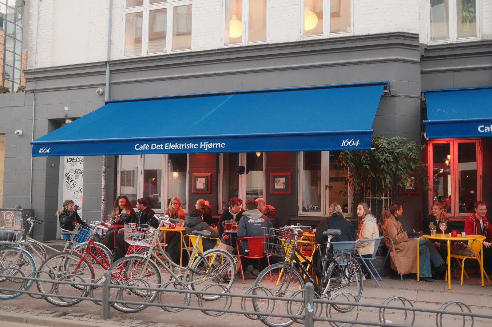 Bicycles parked outside a busy Copenhagen cafe terrace with a blue awning