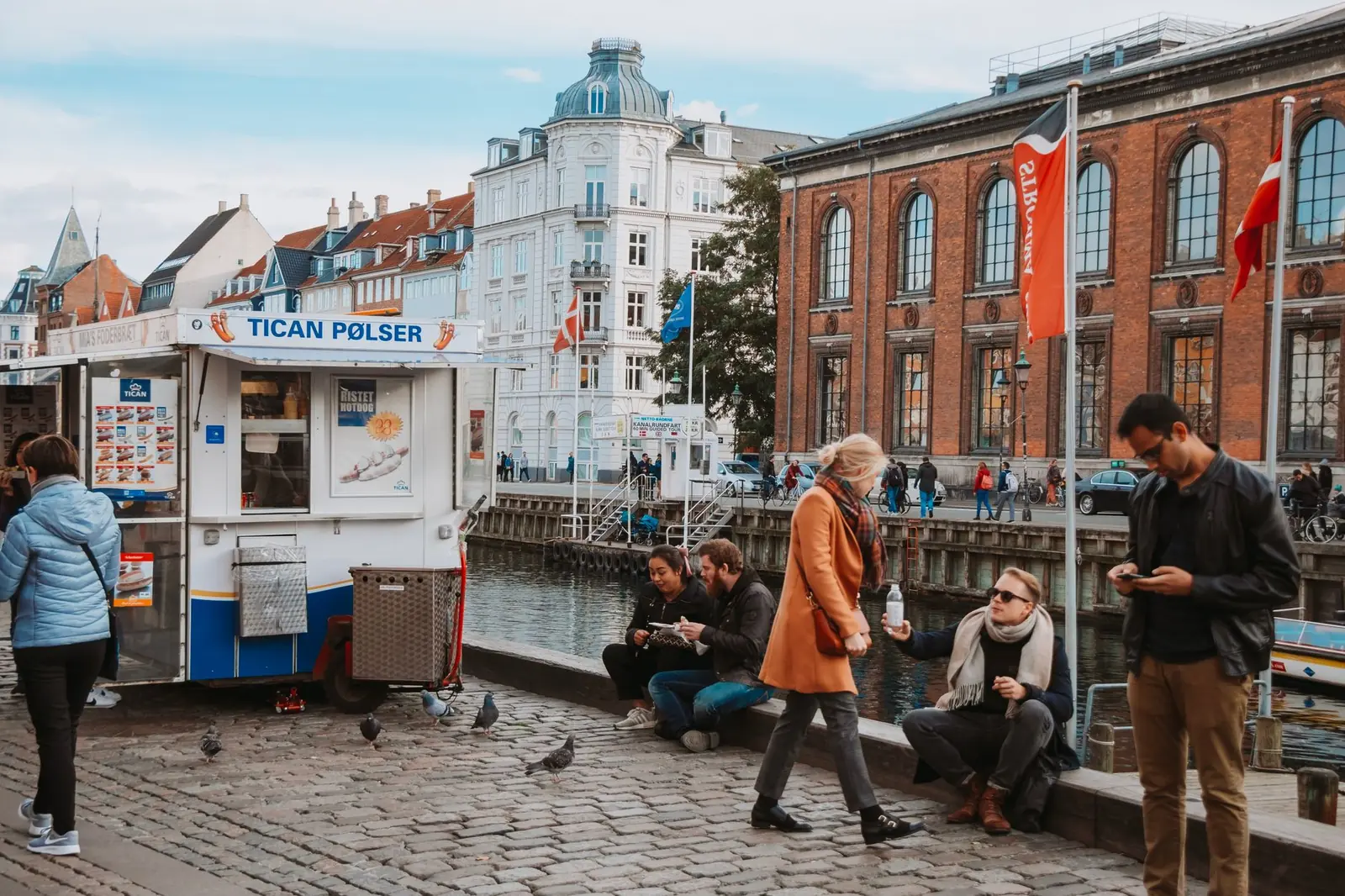 A Danish hot dog van beside a Copenhagen canal with people eating on the quayside