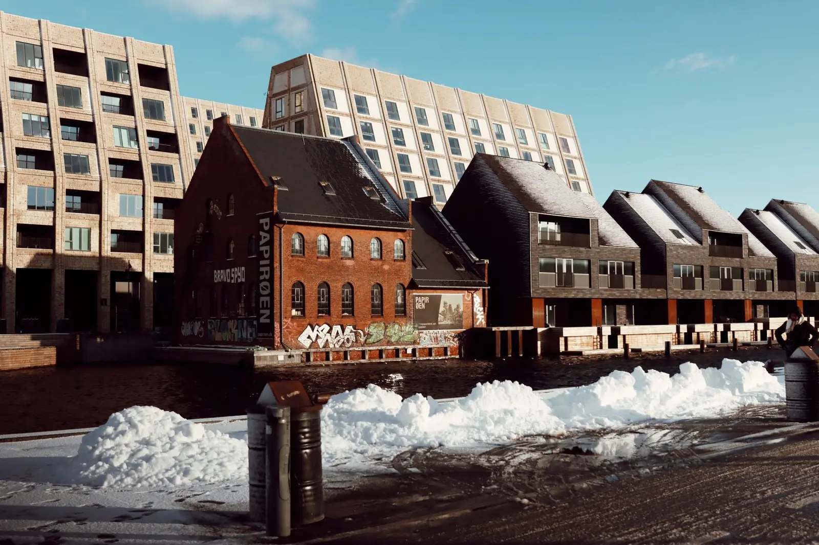 Snow piled along a Copenhagen street beside modern harbourside buildings