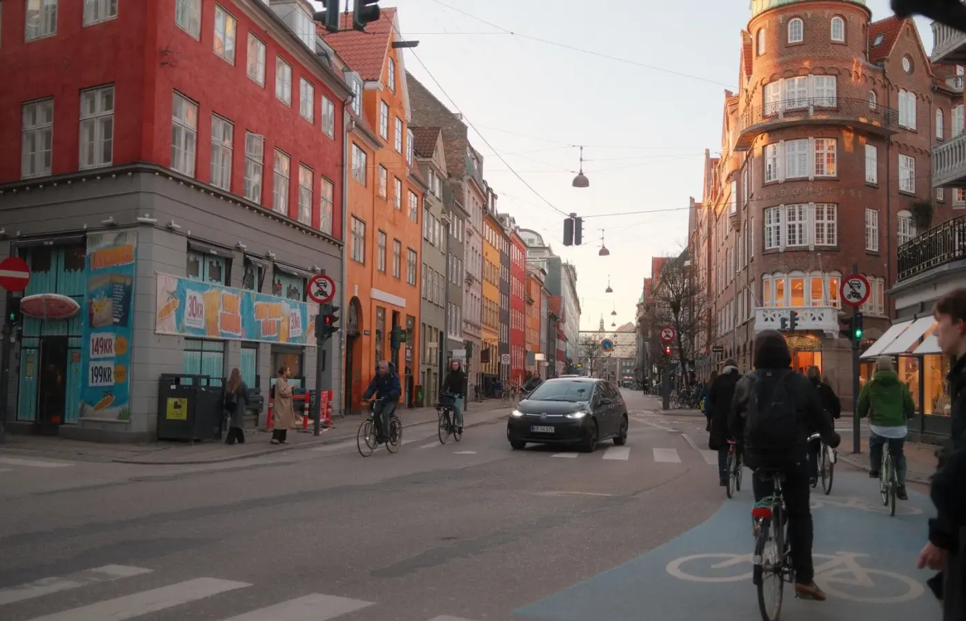 Cyclists riding along a painted cycle lane on a Copenhagen street lined with brick and coloured townhouses