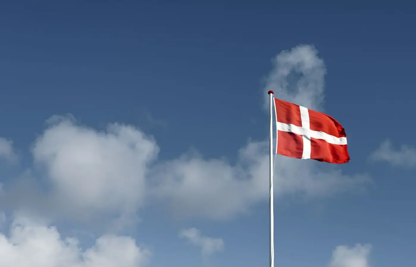 The red and white Danish flag, the Dannebrog, flying from a flagpole against a blue sky