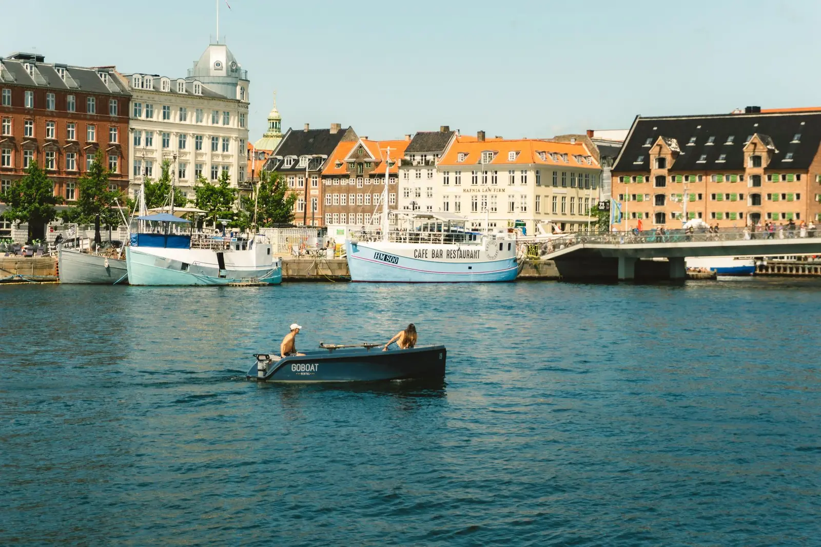 Two people steering a small electric picnic boat across Copenhagen's inner harbour on a sunny day