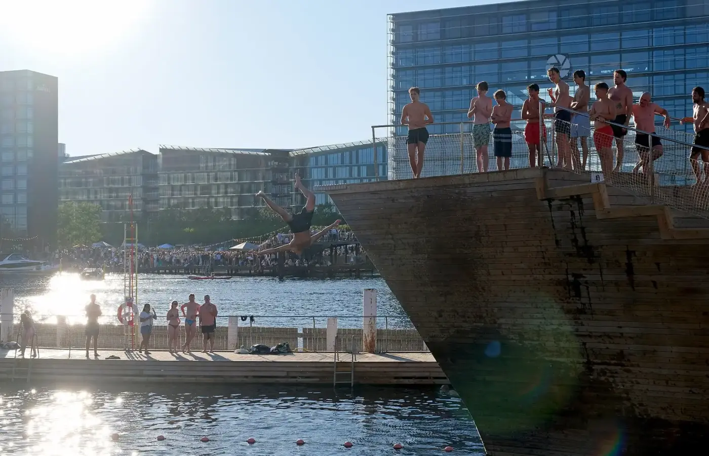 A swimmer diving from the wooden tower at Islands Brygge harbour bath on a sunny summer evening