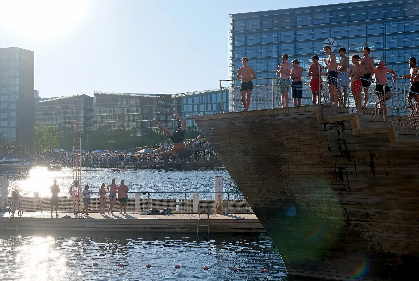 A swimmer diving from the wooden tower at Islands Brygge harbour bath on a sunny summer evening