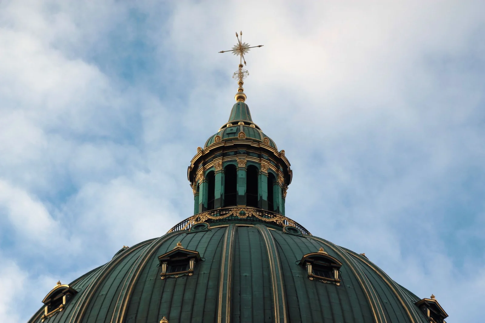 Close view of the Marble Church's green copper dome and lantern against a cloudy sky