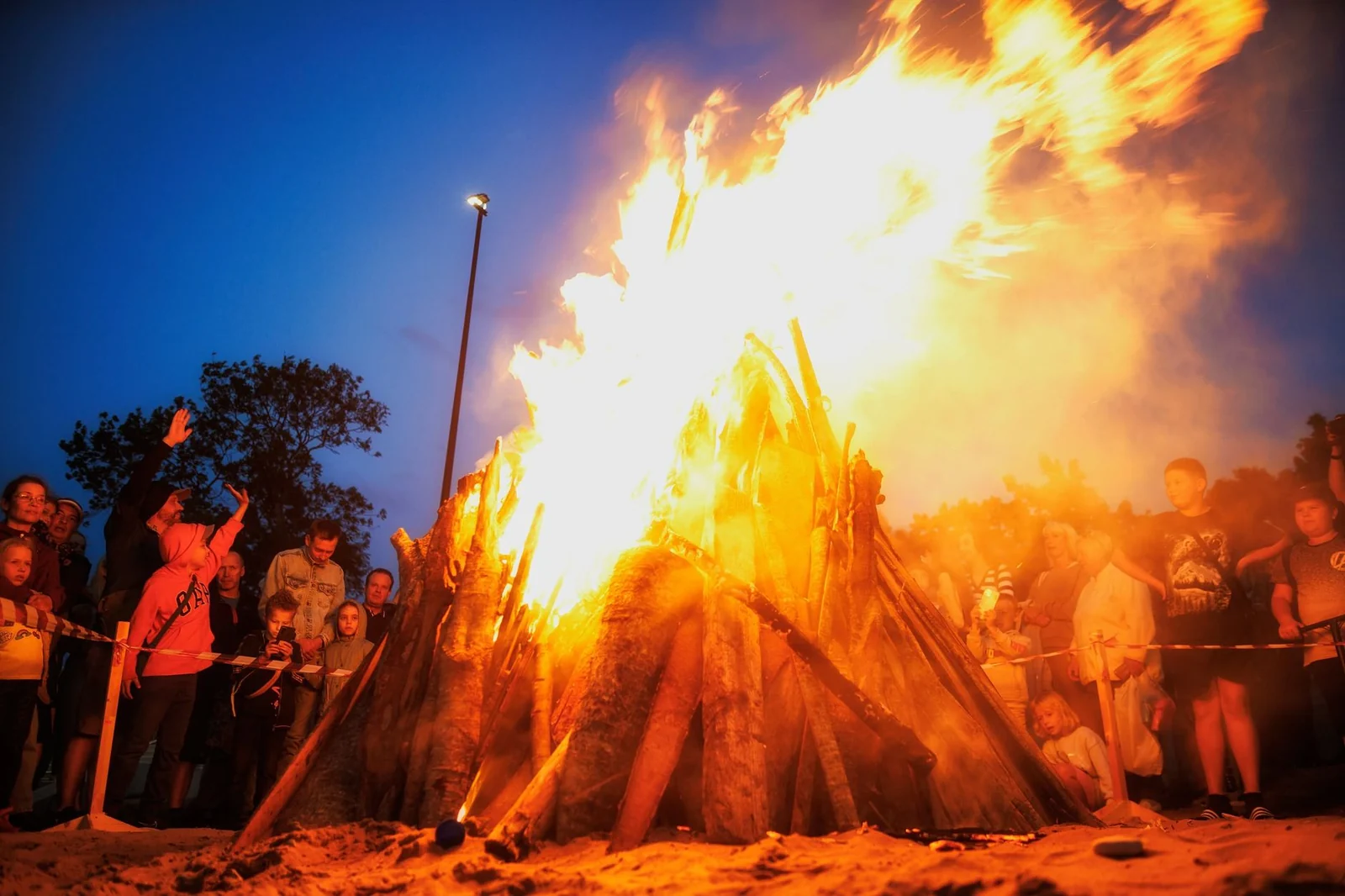 A crowd gathered round a large bonfire on a summer evening