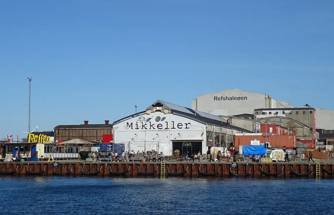 Mikkeller Baghaven's white warehouse on the harbour front of Copenhagen's old shipyard island, with the Reffen street-food sign to the left