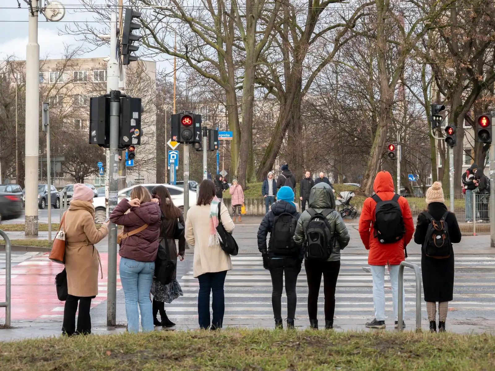A row of pedestrians standing at a red light on an empty crossing