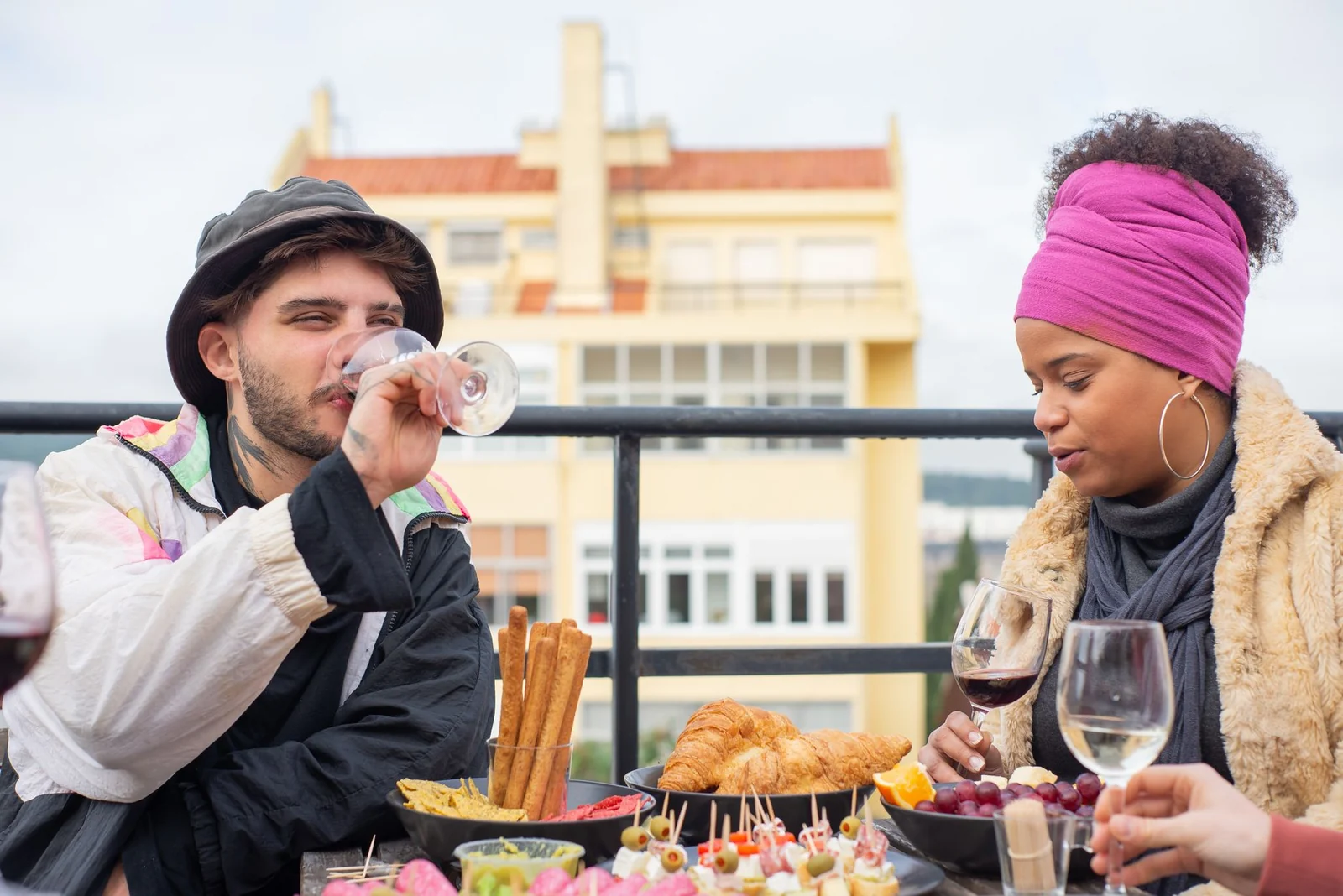 Two people in coats and hats drinking wine at an outdoor rooftop table