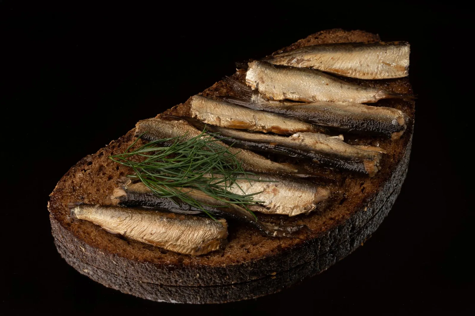 Smoked sprats laid across a slice of dark rye bread with a sprig of dill