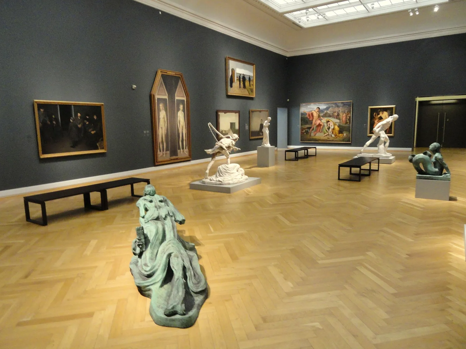 A gallery at SMK with paintings on grey walls and sculptures on a herringbone parquet floor