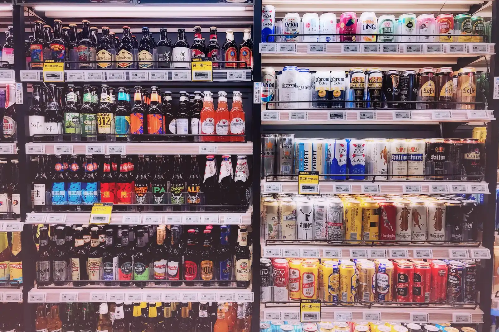 Supermarket beer aisle with bottles and cans stacked on shelves under price labels