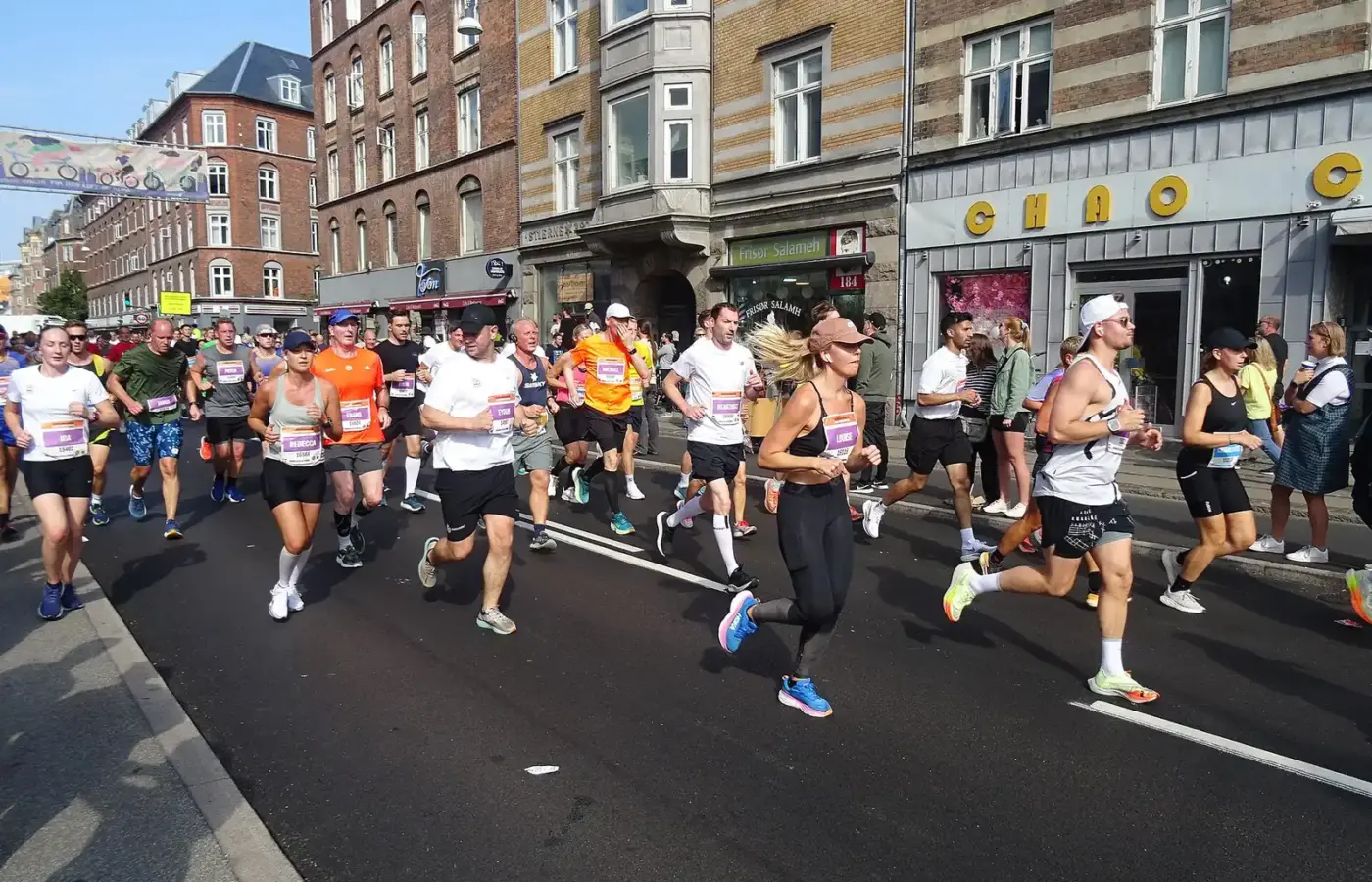 Runners in the Copenhagen Half Marathon passing shops and apartment blocks on a sunny September morning