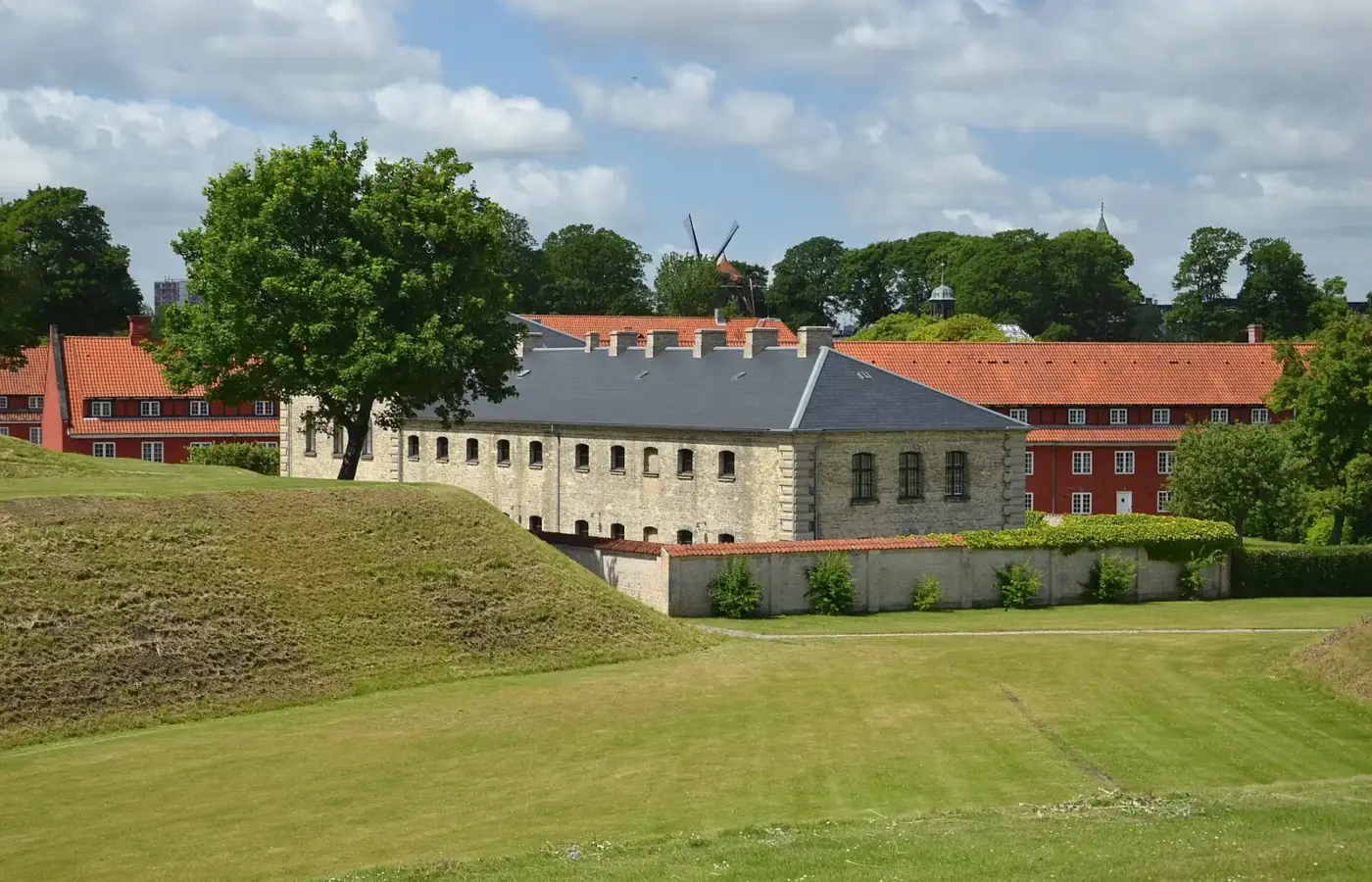 Inside Kastellet: grassy ramparts, red barracks rows and the windmill rising beyond the trees